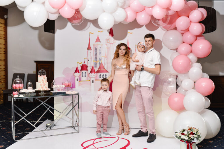 Photo portrait happy parents, family: mother, father, son and daughter on balloons background. Woman, man, boy and little baby girl princess. The concept of a family holiday, birthday celebration.